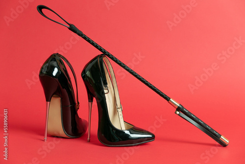 Canvas Print Black shiny high heel shoes and a whip on a red background
