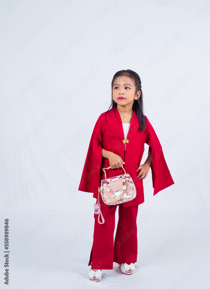 A portrait of a little asian girl wearing red dress, two hands holding a fashion handbag isolated on white background. 