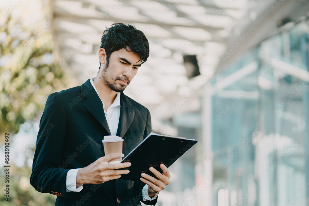Professional businessman using digital tablet computer, smartphone and holding coffee to go while working at office.