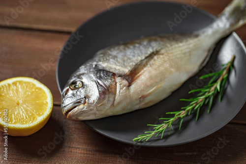 Dorado, raw fresh uncooked fish, source of omega 3, lemon, rosemary, on wooden brown plank table top background, selective focus.