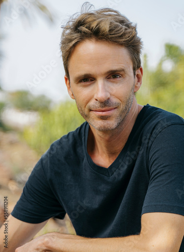 Handsome hipster guy wearing black t-shirt is posing outdoors in a sunny day. He looks happy.
