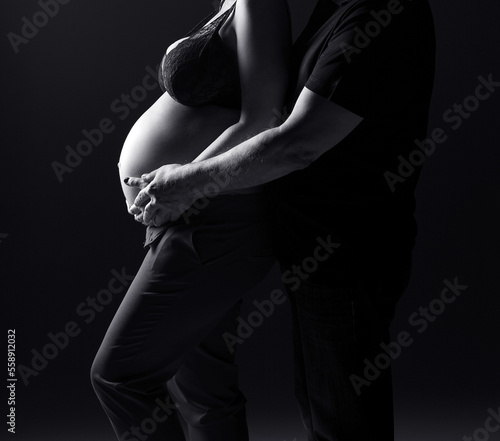 Pregnant couple on a black background. Silhouette of a pregnant woman.Black and white photo. Studio pregnancy photo shoot.