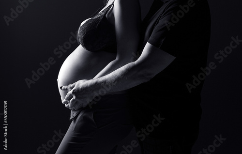 Silhouette of a pregnant woman on a black background. A pregnant couple. A pregnant belly. Black and white photo. Woman holding her belly.