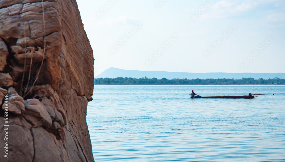 Rocks by the lake, blurred background, fishermen on boats.  Natural scenery that gives a feeling of strength