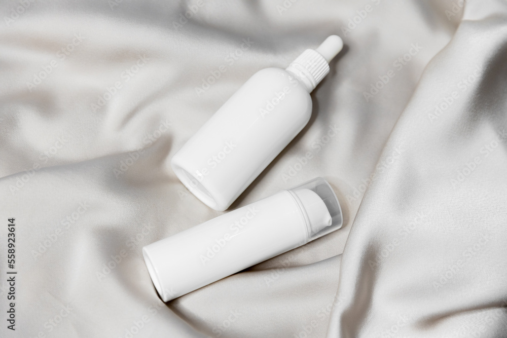 Two white bottles for cosmetics, hair, skin care products without a label on a beige satin background. For beauty salons or cosmetic brands Two white bottles for cosmetics, hair, skin care products without a label on a beige satin background. For beauty salons or cosmetic brands