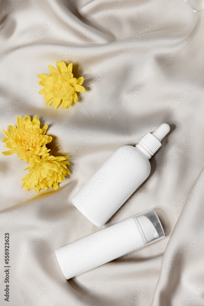 Two white bottles for cosmetics, hair, skin care products without a label on a beige satin background with yellow flowers for decoration Two white bottles for cosmetics, hair, skin care products without a label on a beige satin background with yellow flowers for decoration