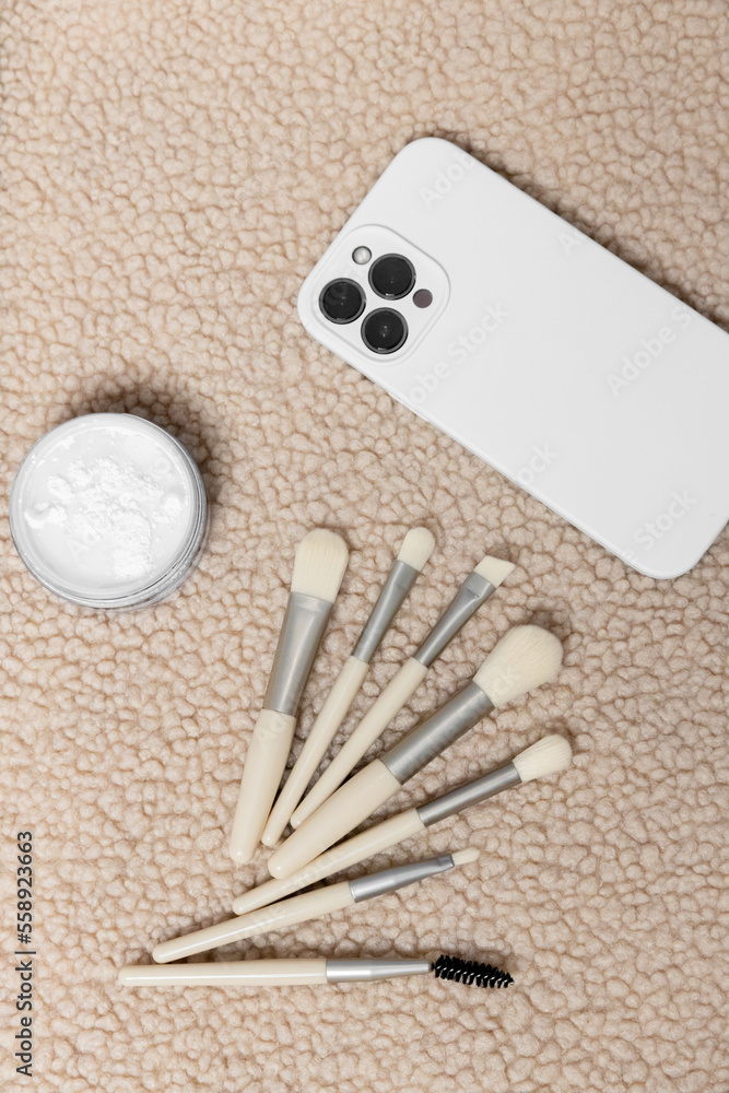 Makeup brushes, cosmetic powder, telephon on a plain textured beige background Makeup brushes, cosmetic powder, telephon on a plain textured beige background