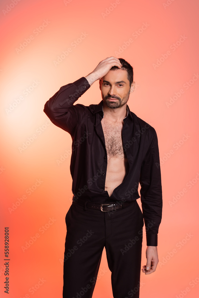 bearded man with hairy chest standing in black outfit and adjusting hair on pink. bearded man with hairy chest standing in black outfit and adjusting hair on pink.