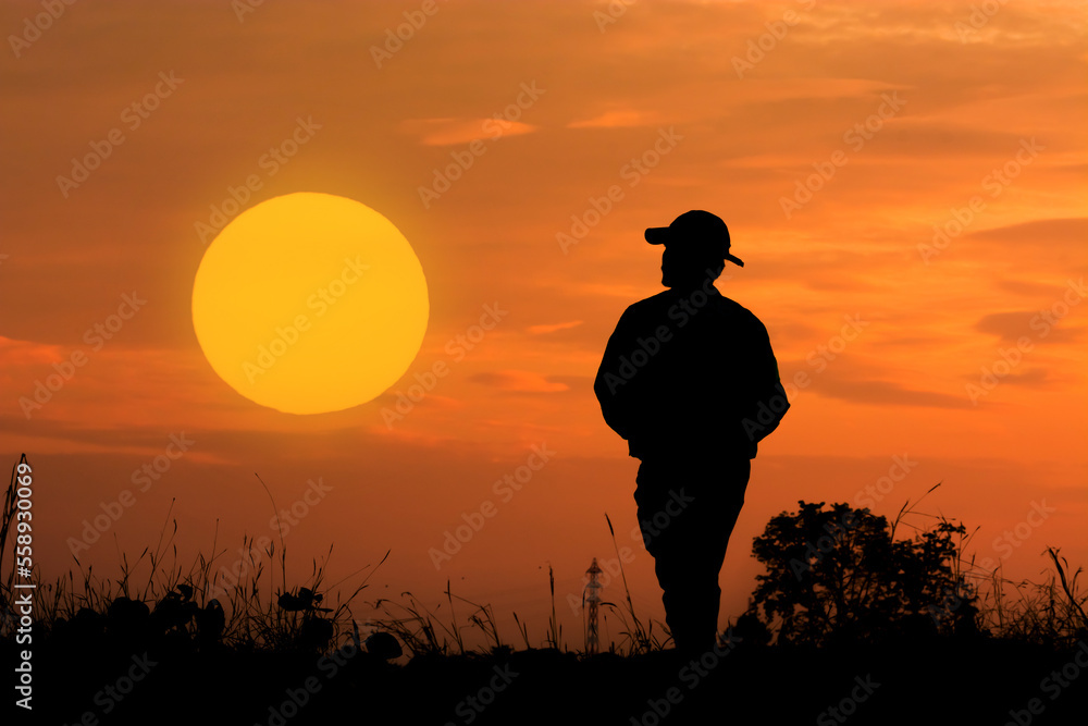 Silhouette of man standing at sunset in nature. Big round sun in background.