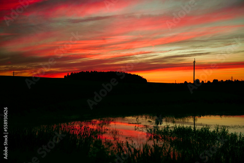 The sky after sunset is the background. A panorama of a colorful magnificent sunset in the countryside over hills, fields and a lake. sunset reflection in the lake. copy space. atmospheric photo © Viktorya 