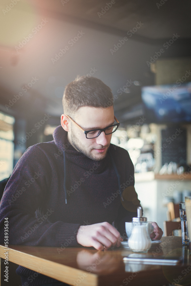 A young man is sitting alone in a cafe, drinking coffee and enjoying himself