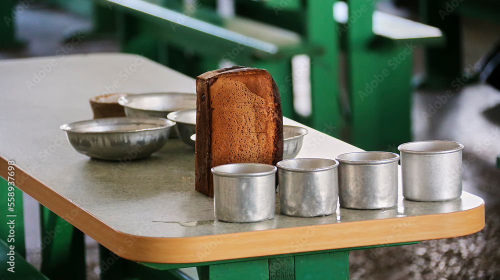 Bread on the table in the dining room of the prison among aluminum mugs and plates. Bread on the table in the dining room of the prison among aluminum mugs and plates.