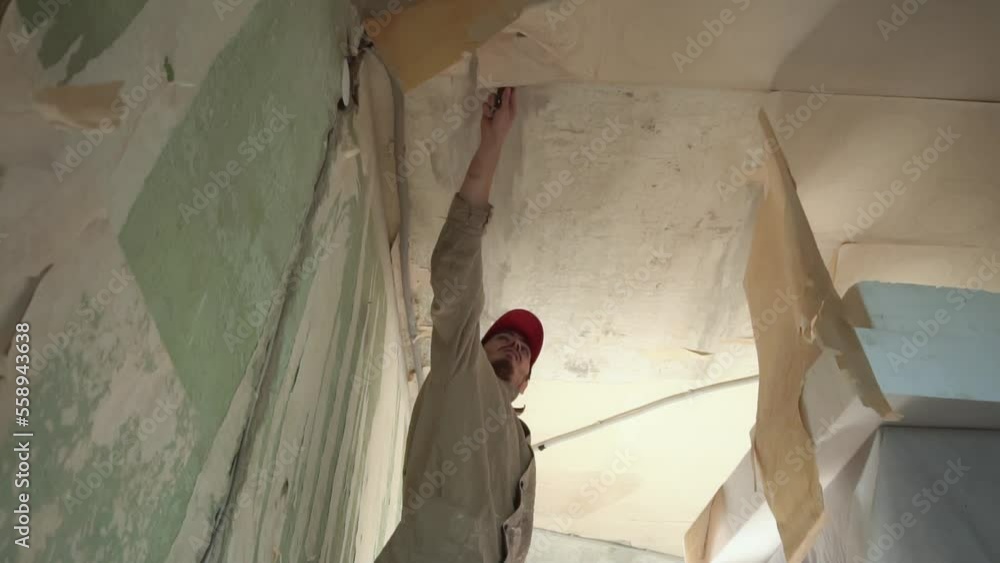 Slow motion of repair man removing wallpaper from ceiling with scraper