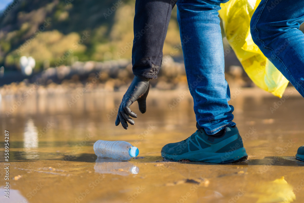 Sea pollution, unrecognizable person walking on the beach collecting plastics. ecology concept Sea pollution, unrecognizable person walking on the beach collecting plastics. ecology concept