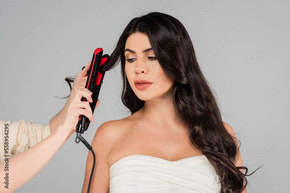 hairdresser styling hair of pretty woman with hair straightener isolated on grey. hairdresser styling hair of pretty woman with hair straightener isolated on grey.