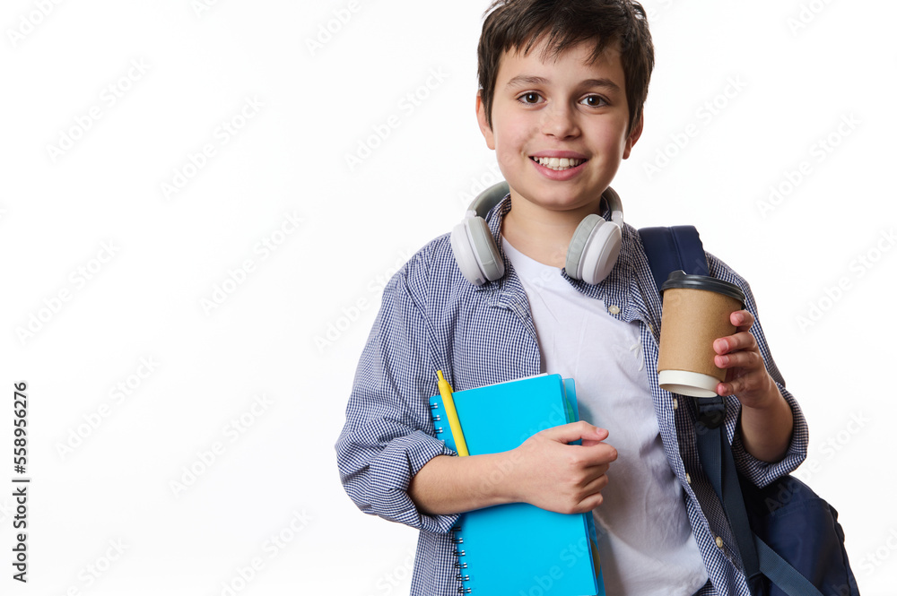 Caucasian smiling teenage schoolboy with school supplies and backpack, holding out a takeaway drink in disposable paper cup, looking at camera, isolated on white background. Copy advertising space Caucasian smiling teenage schoolboy with school supplies and backpack, holding out a takeaway drink in disposable paper cup, looking at camera, isolated on white background. Copy advertising space