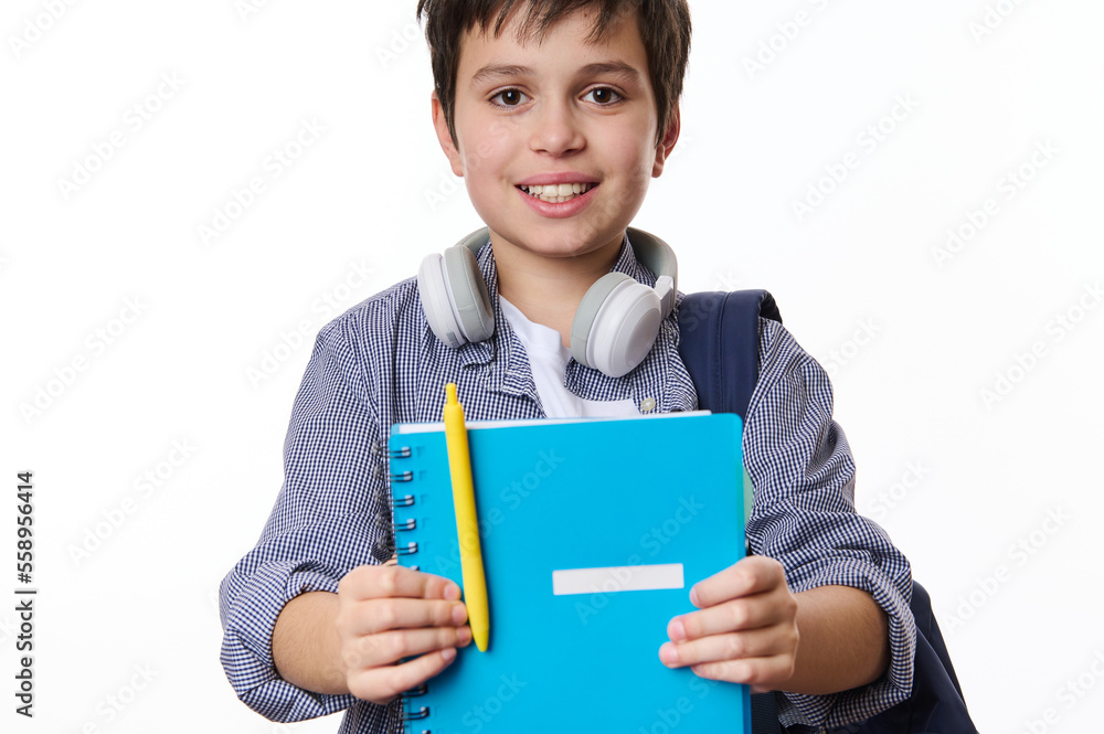Adorable teen boy, primary school student holding out a blue copybook and yellow pen, smiling a cute toothy smile looking at camera, isolated over white background. Back to school on new academic year Adorable teen boy, primary school student holding out a blue copybook and yellow pen, smiling a cute toothy smile looking at camera, isolated over white background. Back to school on new academic year