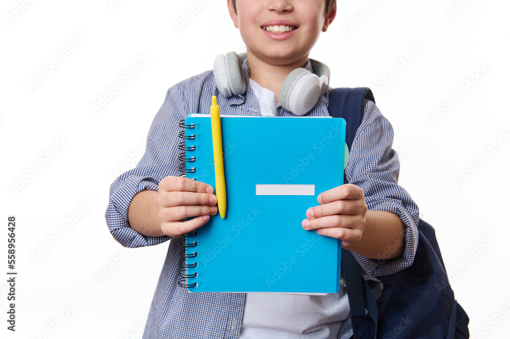 Focus on a blue copybook with yellow pen in hands of a cheerful teenage school boy, wearing casual wear, smiling a toothy smile, isolated on white background, copy space. School and education concept Focus on a blue copybook with yellow pen in hands of a cheerful teenage school boy, wearing casual wear, smiling a toothy smile, isolated on white background, copy space. School and education concept