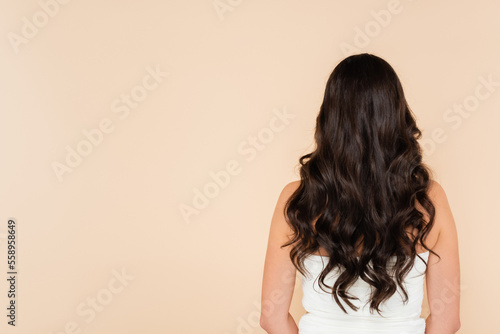 Back view of curly brunette woman standing isolated on beige.
