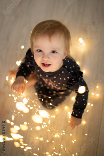 Happy smiling caucasian baby girl with lights garland sitting on the floor photo