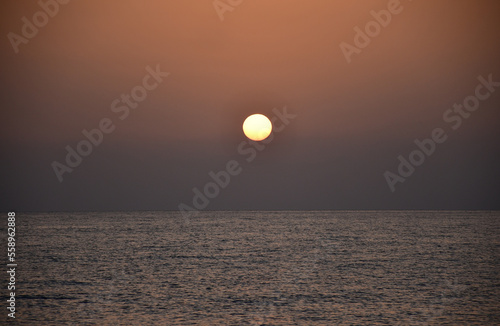 Fototapeta Naklejka Na Ścianę i Meble -  The sun rises over the sea from behind the mountains. ripples on the surface of the water. Dawn in dark colors. Round sun without rays
