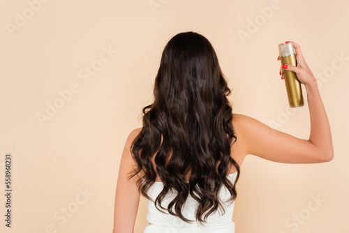 Back view of woman with wavy hairstyle using hairspray isolated on beige. photo