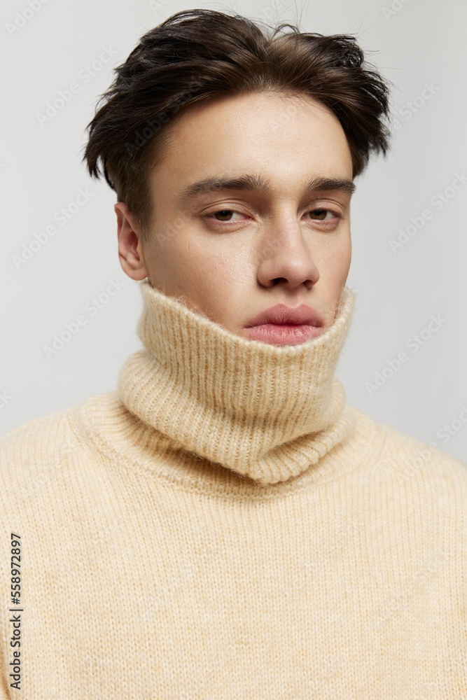Portrait photo. vertical studio. close-up photo.Cute young man with dark combed back short curly hair in a beige sweater with a high neck stands on a gray background vertical studio photo Portrait photo. vertical studio. close-up photo.Cute young man with dark combed back short curly hair in a beige sweater with a high neck stands on a gray background vertical studio photo