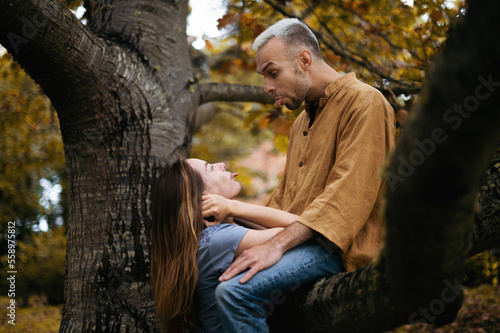 A playful and romantic photo of a young couple in a beautiful autumn park, with the man sitting on a tree