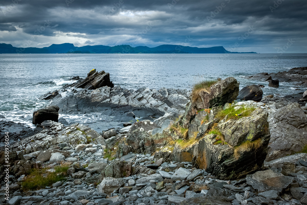 Jagged rocks with moss adorn the rugged coastline under a stormy sky at evening.