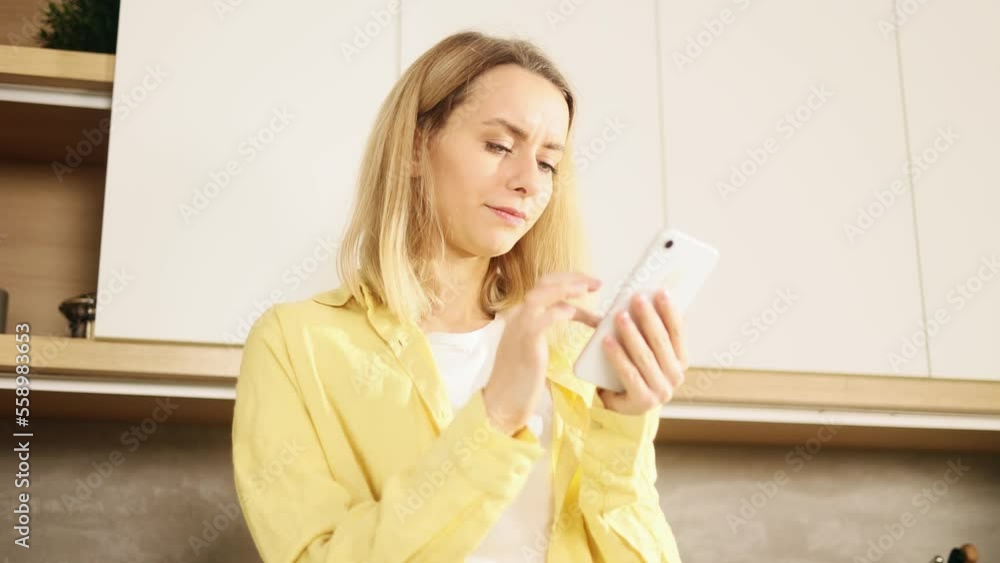Boring young blond woman scrolling feed of social networks products in internet store or recipes on smartphone in kitchen Tired exhausted felale look at mobile screen without enthusiasm at home Boring young blond woman scrolling feed of social networks products in internet store or recipes on smartphone in kitchen Tired exhausted felale look at mobile screen without enthusiasm at home