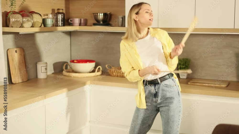 Portrait of attractive cheerful blond woman have fun with energetic dance at domestic kitchen in slow motion Young housewife dancing with spoon and enjoying leisure time at home alone Portrait of attractive cheerful blond woman have fun with energetic dance at domestic kitchen in slow motion Young housewife dancing with spoon and enjoying leisure time at home alone