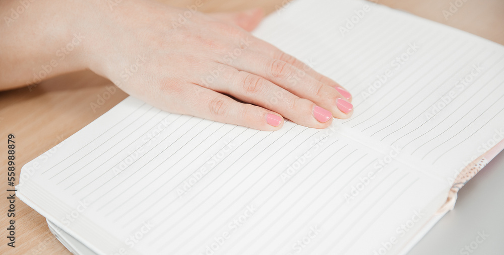 Close up of a woman's hands writing in a notepad placed on a wooden table, home office and work concept, plans and thoughts Close up of a woman's hands writing in a notepad placed on a wooden table, home office and work concept, plans and thoughts