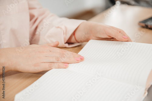 Close up of a woman's hands writing in a notepad placed on a wooden table, home office and work concept, plans and business meeting