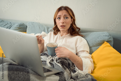 Dejected female with notebook computer and cup in bedroom