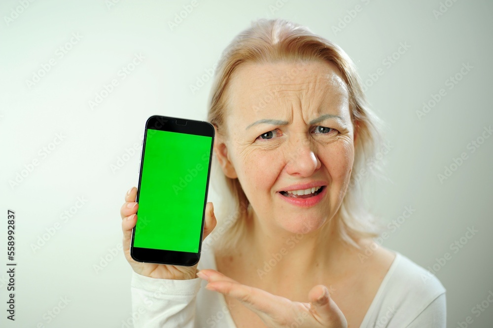 woman is dissatisfied, she moved her eyebrows forehead wrinkled and moved her mouth points to the phone with a green chroma key screen place for text She is on a white background in the studio woman is dissatisfied, she moved her eyebrows forehead wrinkled and moved her mouth points to the phone with a green chroma key screen place for text She is on a white background in the studio