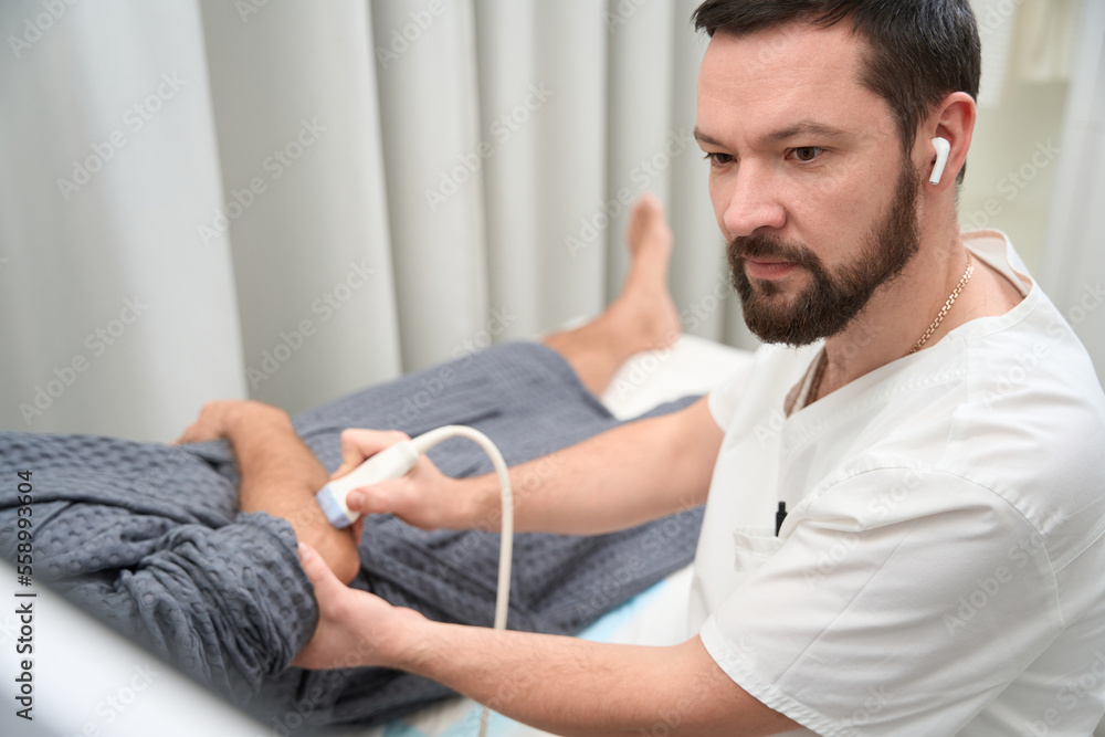 Concentrated therapist doing an ultrasonography of person elbow Concentrated therapist doing an ultrasonography of person elbow