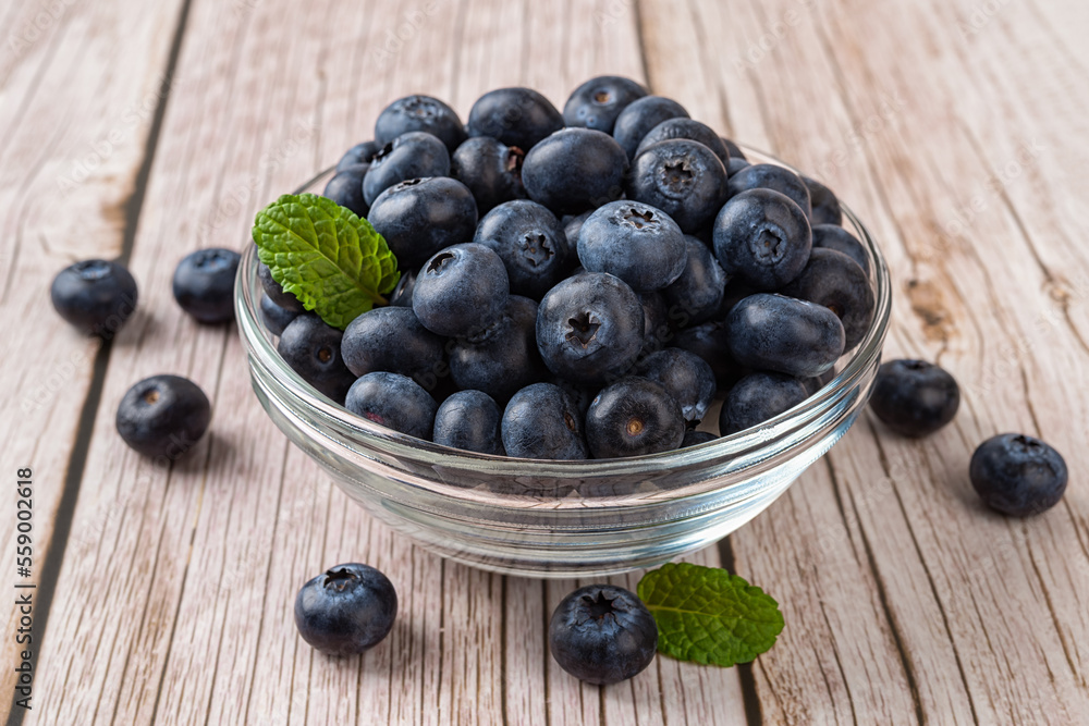 Ripe blueberry in a glass bowl over wooden background. Fresh blueberries for vegetarian dessert. Wild berry for natural antioxidant and healthy eating concept. Vitamin vegan snack. Ripe blueberry in a glass bowl over wooden background. Fresh blueberries for vegetarian dessert. Wild berry for natural antioxidant and healthy eating concept. Vitamin vegan snack.