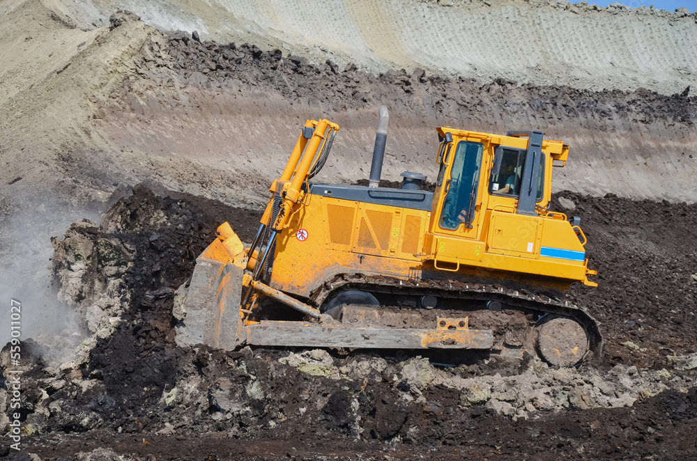 Obraz premium Crawler bulldozer working on construction site or quarry. Mining machinery moving clay, smoothing gravel surface for new road. Earthmoving, excavations, digging on soils