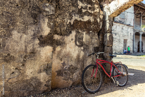 Bicicleta roja apoyada en muro antiguo.