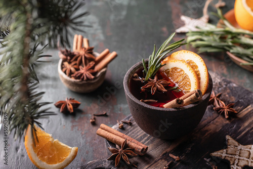Mulled red wine in ceramic bowl with spices, fruits and rosemary on wooden rustic table, dark key. Traditional hot drink at Christmas time and winter