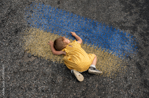 A little girl lies on the asphalt on which the flag of Ukrina is drawn with chalk