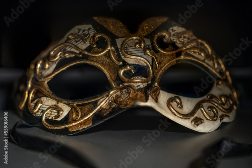 image of a golden Venetian mask with pieces of musical score and black ribbons on a dark background