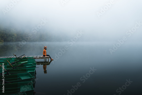Canvas Print Side view of fashioned young woman sitting on wooden dock looking at view on a misty morning