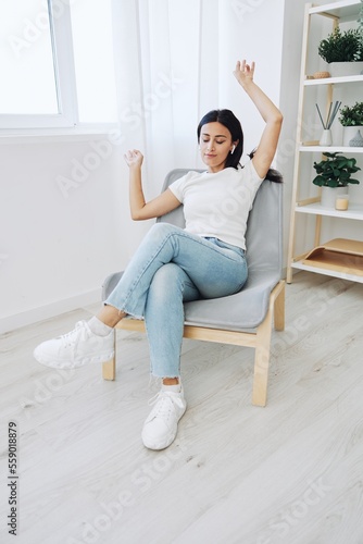 Woman sitting in a chair listening to music and dancing with wireless headphones at home in jeans and a white T-shirt, fall lifestyle comfort © SHOTPRIME STUDIO