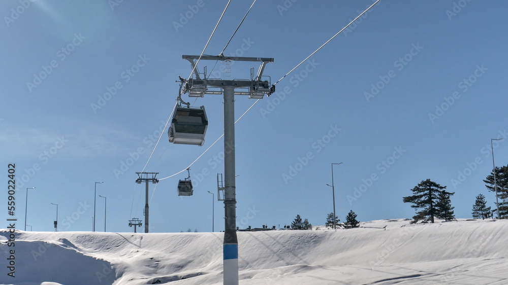 Gondola lift - cable car in the mountain tourist center. Snow covered ground, blue sky, sunny day Gondola lift - cable car in the mountain tourist center. Snow covered ground, blue sky, sunny day