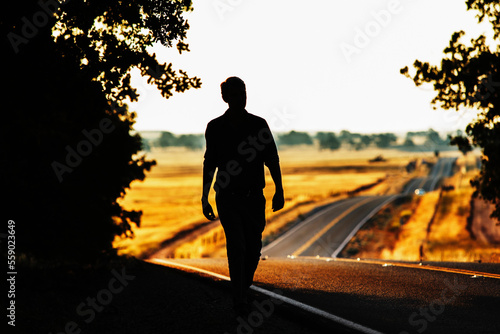 A silhouetted man walking along side of a country road. photo