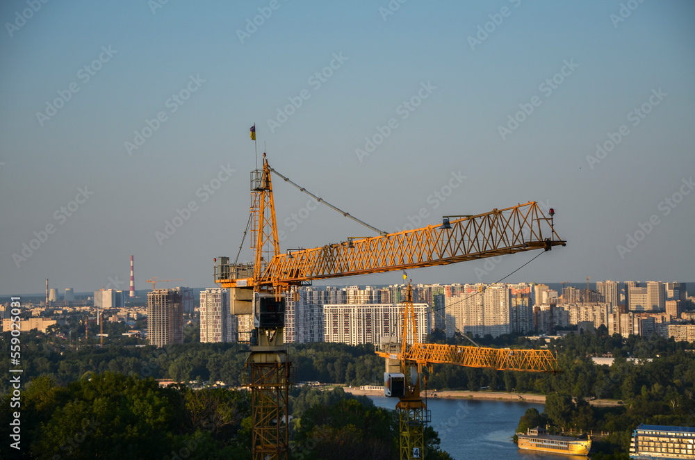 Two high construction cranes with Dnipro river and left bank city districts on the background. Urban skyline of Kyiv, Ukraine 