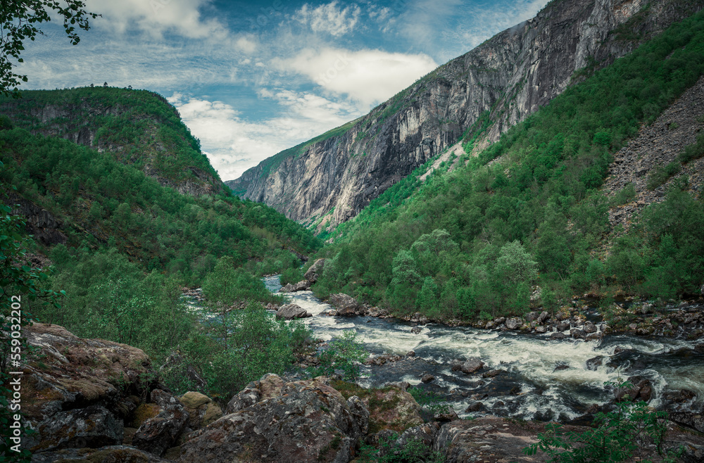 River currents in the valley of Voringsfossen waterfall at Hardangervidda National Park in Norway, steep mountains aside, green vegeation