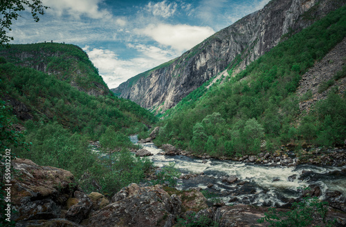 River currents in the valley of Voringsfossen waterfall at Hardangervidda National Park in Norway, steep mountains aside, green vegeation