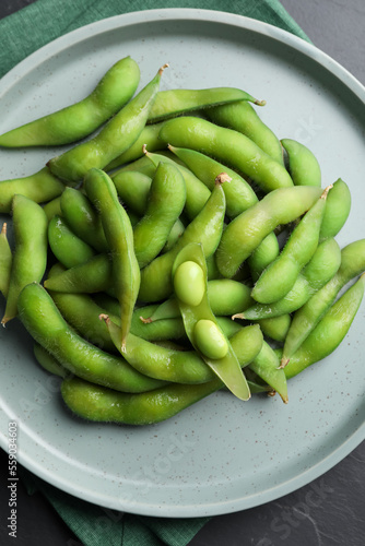 Plate of green edamame beans in pods on black table, top view